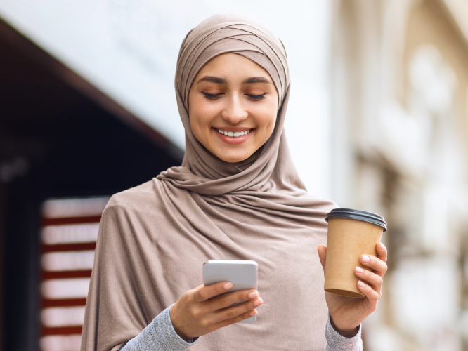 Muslim girl smiling with coffee and handphone
