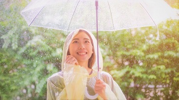 Seorang wanita memakai baju hujan sambil memegang payung